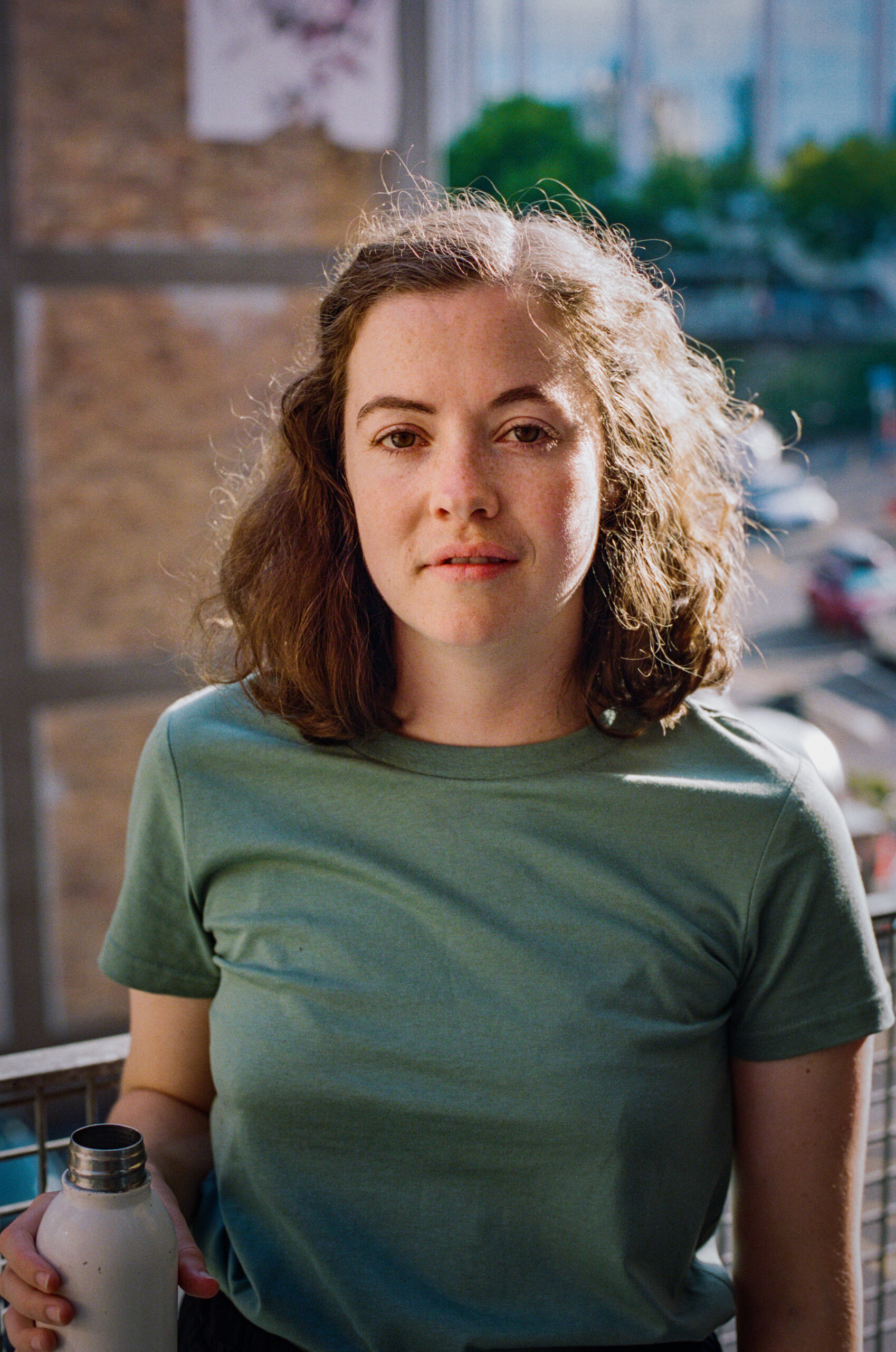2021-02 - Feb to Apr20 Clare holds a drink bottle and wears a sage green tshirt. She has mid length brown hair and freckles.
