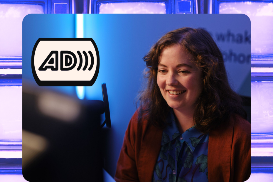 Clare sits at a computer next to a microphone. A logo for Audio Description is on the left, with a blue background behind her